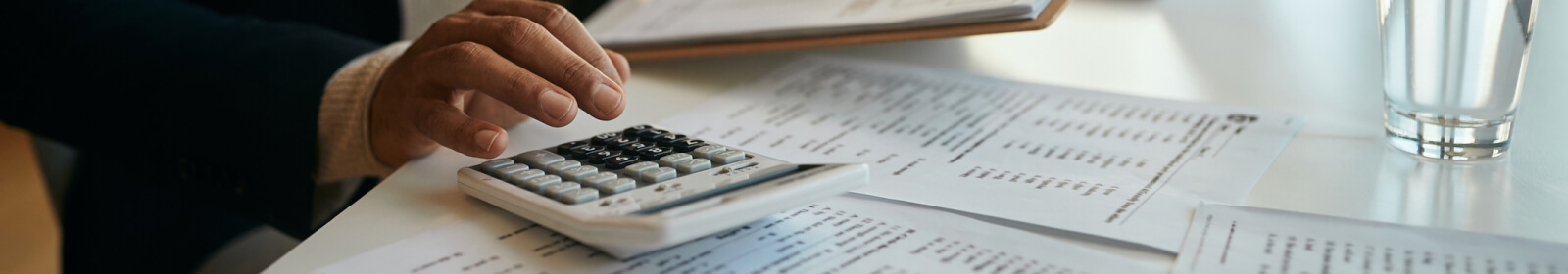 A persons hand using a calculator that is placed on a desk of financial statements