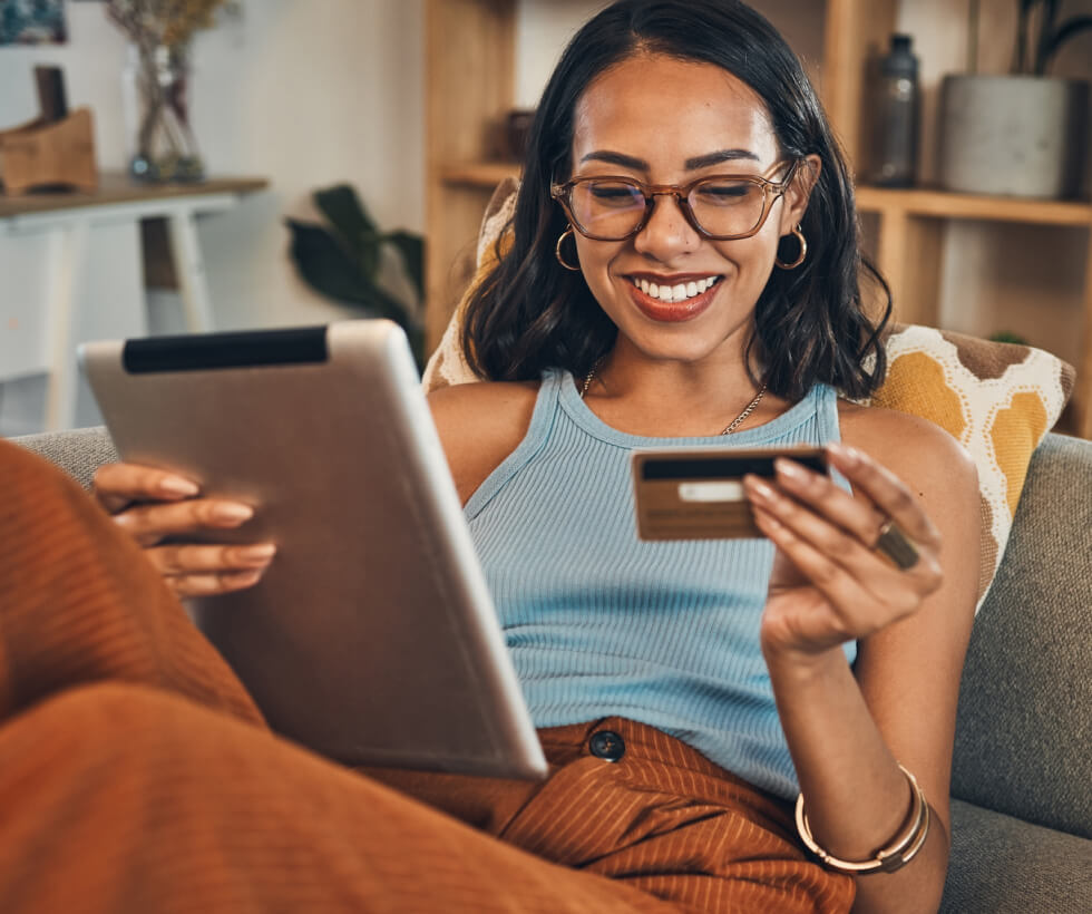 Woman relaxing on couch while smiling and holding her tablet and credit card